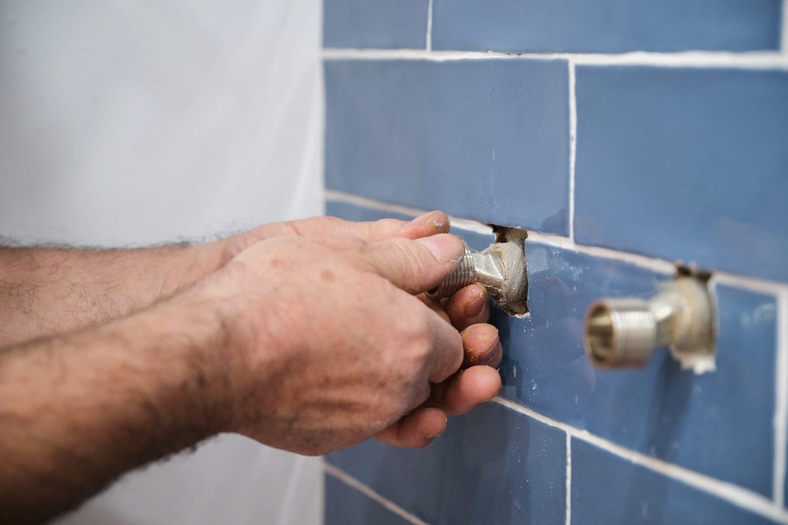 Plumber's hands installing pipe fittings in wall
